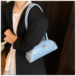 Detail of light blue crocodile embossed cylindrical shoulder bag with metal logo plate