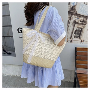 Close-up of beige straw bag featuring intricate white lace crochet and a large bow detail