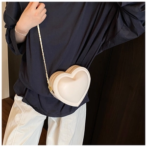 Détail du sac à bandoulière en forme de cœur blanc crème avec chaîne dorée sur mannequin