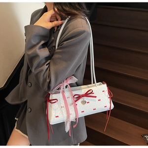 Detail of white baguette bag featuring red bow patterns and heart-shaped metal pendant