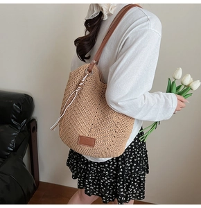 Detail of woven straw tote bag with brown leather strap held by model in summer dress
