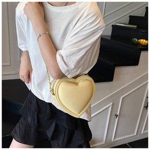 Détail d'un sac bandoulière beige chic en forme de cœur avec chaîne dorée sur mannequin