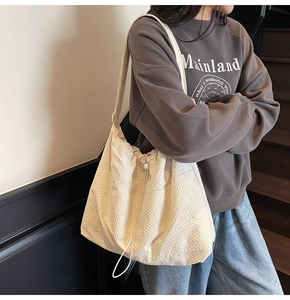 Detailed shot of cream textured tote bag with drawstring closure worn by a model