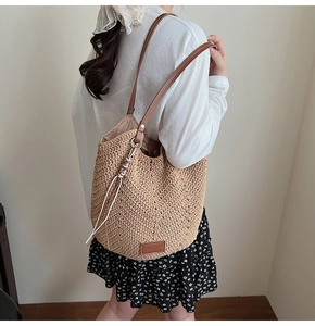 Detail view of woven straw tote bag with brown leather straps and bottom logo patch