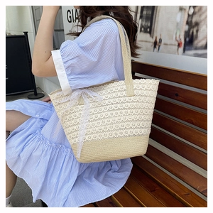Detail view of woven straw beach bag featuring intricate lace stitching and side bow