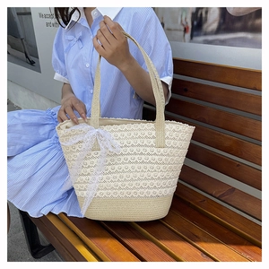 Detailed shot of beige straw tote bag with delicate white lace and side bow detail