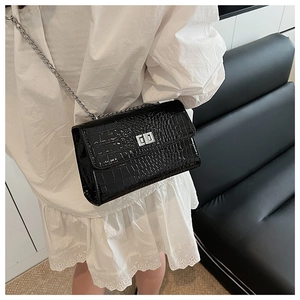Detail of black crocodile texture bag with silver chain strap on a model's shoulder
