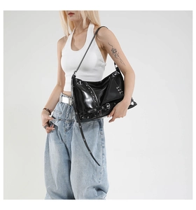 Detail of black glossy tote bag with metal studs and buckle straps in a punk style