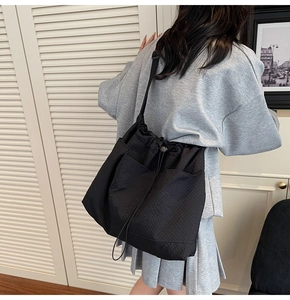Detail view of a black pleated canvas tote bag with side pockets on a model