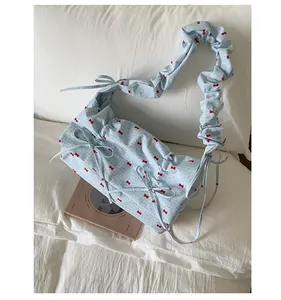 Détail du sac floral bleu clair avec motifs nœuds rouges et bandoulière froncée