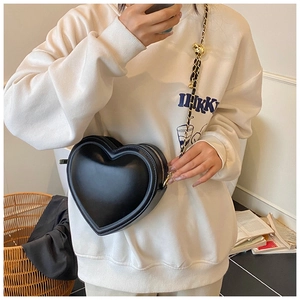 Détail d'un sac bandoulière noir en forme de cœur avec chaîne dorée sur un mannequin