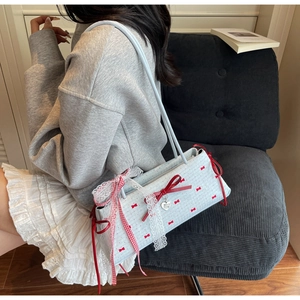Detail of light blue plaid shoulder bag with red bows and lace trim on a model