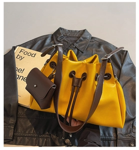 Detail of yellow drawstring bucket bag with brown strap on a black leather jacket