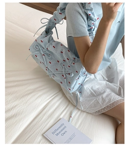 Détail du sac floral bleu clair avec imprimés nœuds rouges et bandoulière à volants