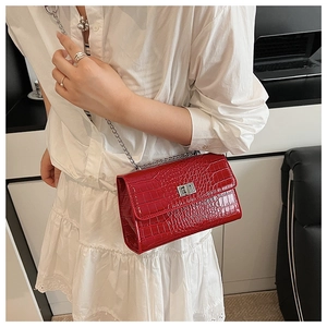 Detail of red croc-embossed crossbody bag featuring silver turn-lock and chain strap
