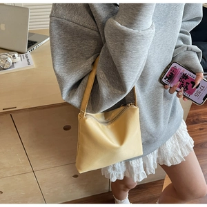 Gros plan d'un sac à bandoulière jaune pâle avec fermeture éclair et texture minimaliste