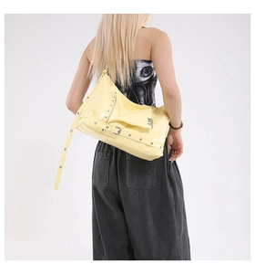 Detail of pale yellow patent leather tote with silver rivets and glossy finish on model