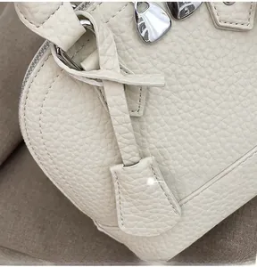 Makro-Detail der cremeweißen Handtasche mit Lychee-Narbenleder und silbernen Reißverschlüssen