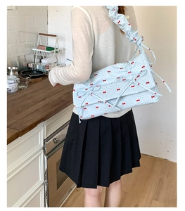 Modèle portant un sac plissé bleu clair avec des nœuds rouges dans un décor de maison