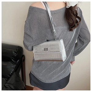 Detail of silver crocodile-patterned crossbody bag with metal chain strap and twist lock