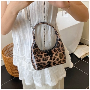 Detail of glossy leopard print patent leather handbag with silver chain strap worn by a model