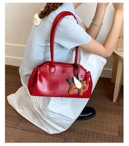 Détail d'un sac bowling rouge brillant avec poignées fines et charm de Pégase