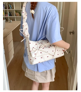 Détail de la bandoulière d'un sac en toile blanc avec motifs de nœuds rouges brodés