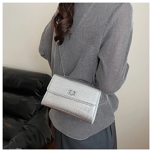 Detail showing silver crocodile pattern leather bag with chain strap on a shoulder