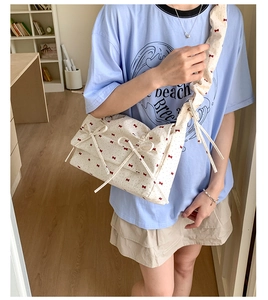 Détail d'un sac à fleurs avec nœuds rouges et large bandoulière plissée sur un modèle