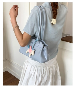 Détail du sac à bandoulière en cuir verni bleu clair avec breloque poney rose et logo gaufré