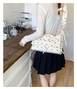Détail du sac crème à fleurs avec nœuds rouges et bandoulière plissée élégante