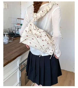 Détail du sac à bandoulière beige avec imprimé nœuds rouges et texture plissée nuage