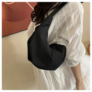 Detail of large black hobo shoulder bag with textured fabric worn on a white dress