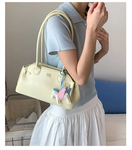 Sac bowling en cuir crème avec breloque licorne porté avec une tenue d'été décontractée