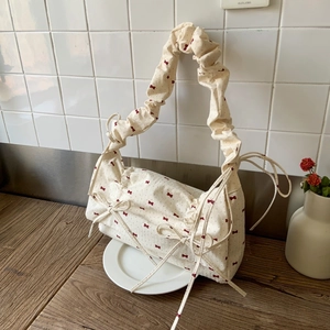 Floral fabric shoulder bag with red bow prints and ruffled cloud strap on wooden table
