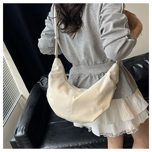Detail of a creamy white crescent bag featuring vertical pleated texture on a shoulder strap