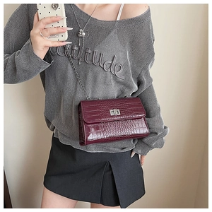 Detail of burgundy crocodile-embossed bag with silver turn-lock and chain strap