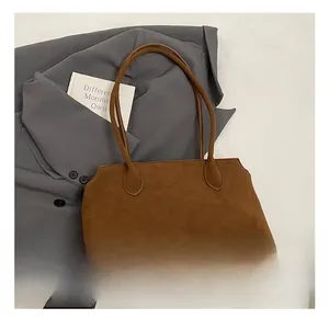 Top-down view of a dark brown suede tote bag with minimalist slim handles on grey suit