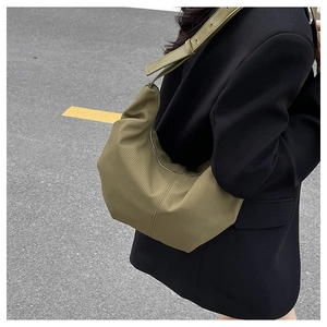 Close-up of olive green dumpling bag with pleated texture worn by a model in a suit