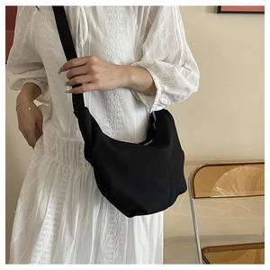 Detail of minimalist black crescent crossbody bag with textured fabric on a white dress