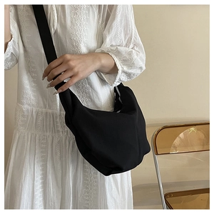 Minimalist large black dumpling bag with wide strap worn with white dress