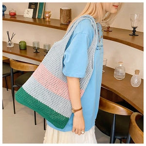 Detail view of a large woven tote bag with a striped color-block design in a cafe setting