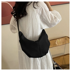 Detail view of a black nylon crescent bag worn crossbody with casual drapery
