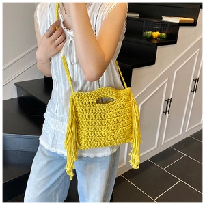 Close-up of yellow hand-woven knit crossbody bag featuring decorative side tassels
