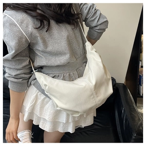 Close-up of white pleated crescent bag with vertical textures and silver metal zipper details