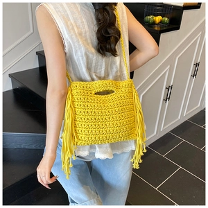 Close-up of a yellow hand-knitted crossbody bag featuring crochet tassels and hollow handle