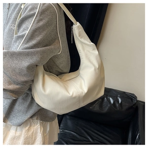 Detail of white pleated hobo bag showing textured crescent shape and wide shoulder strap