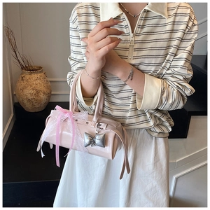 Détail du sac à main en cuir verni rose clair avec nœud en dentelle et breloque papillon