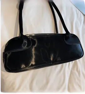 Détail du sac à bandoulière en cuir verni noir brillant avec bretelles fines et design rétro