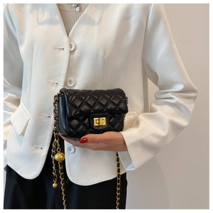 Detail van een zwarte gewatteerde crossbodytas met gouden ketting op een wit jasje